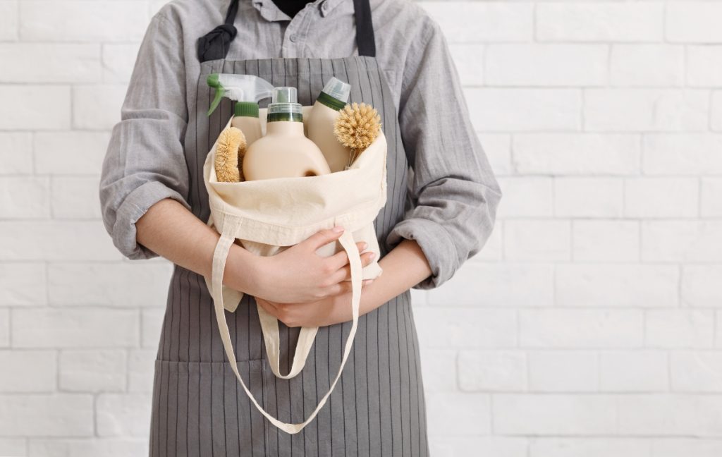A man in an apron holding a satchel full of hotel hygiene and sustainability cleaning products.